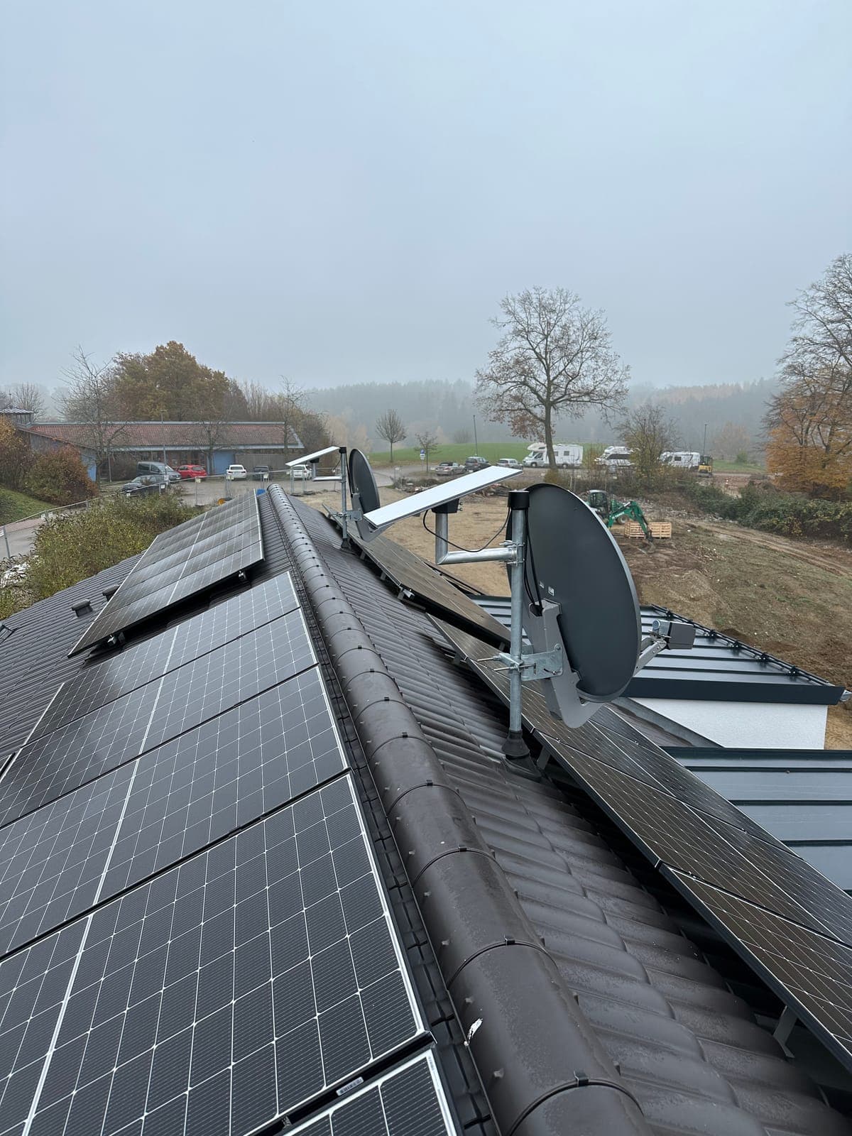 Starlink-Antenne auf Masthalterung am First eines Ziegeldachs neben Solarmodulen